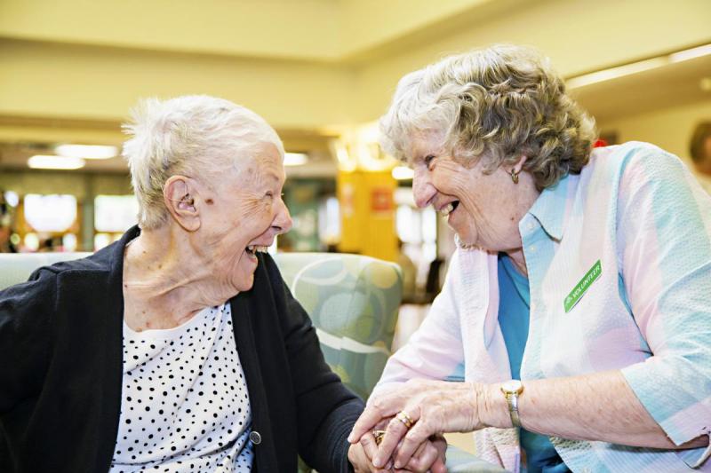 Volunteer and resident sitting holding hands, and laughing together