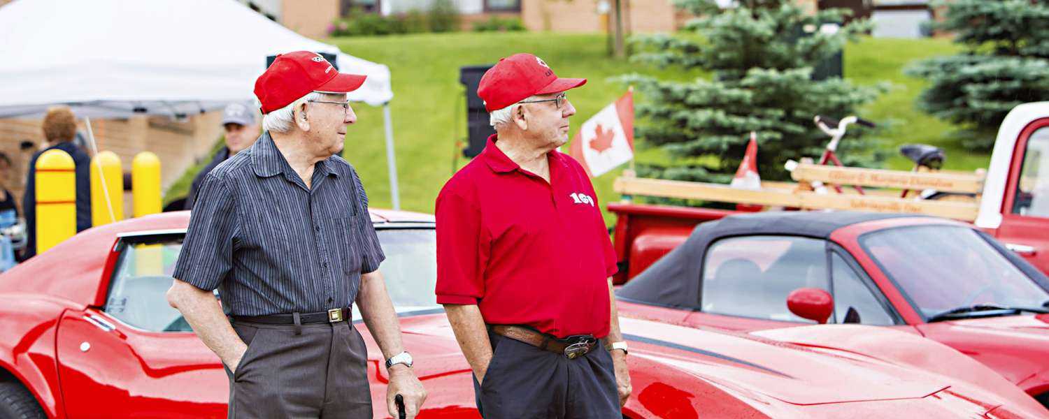 Two gentlemen standing beside red classic cars